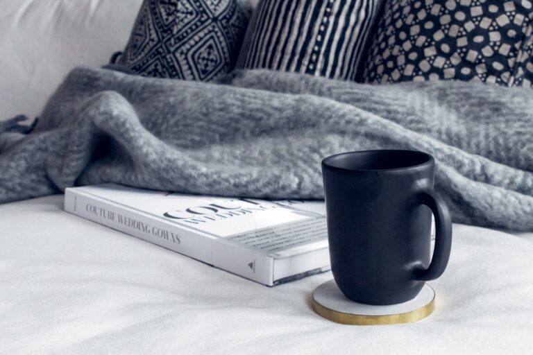 Bilden visar en pläd tillsammans med en bok och en kaffekopp. Plädar värmer skönt och skapar ett mysigare hem med enkla medel.